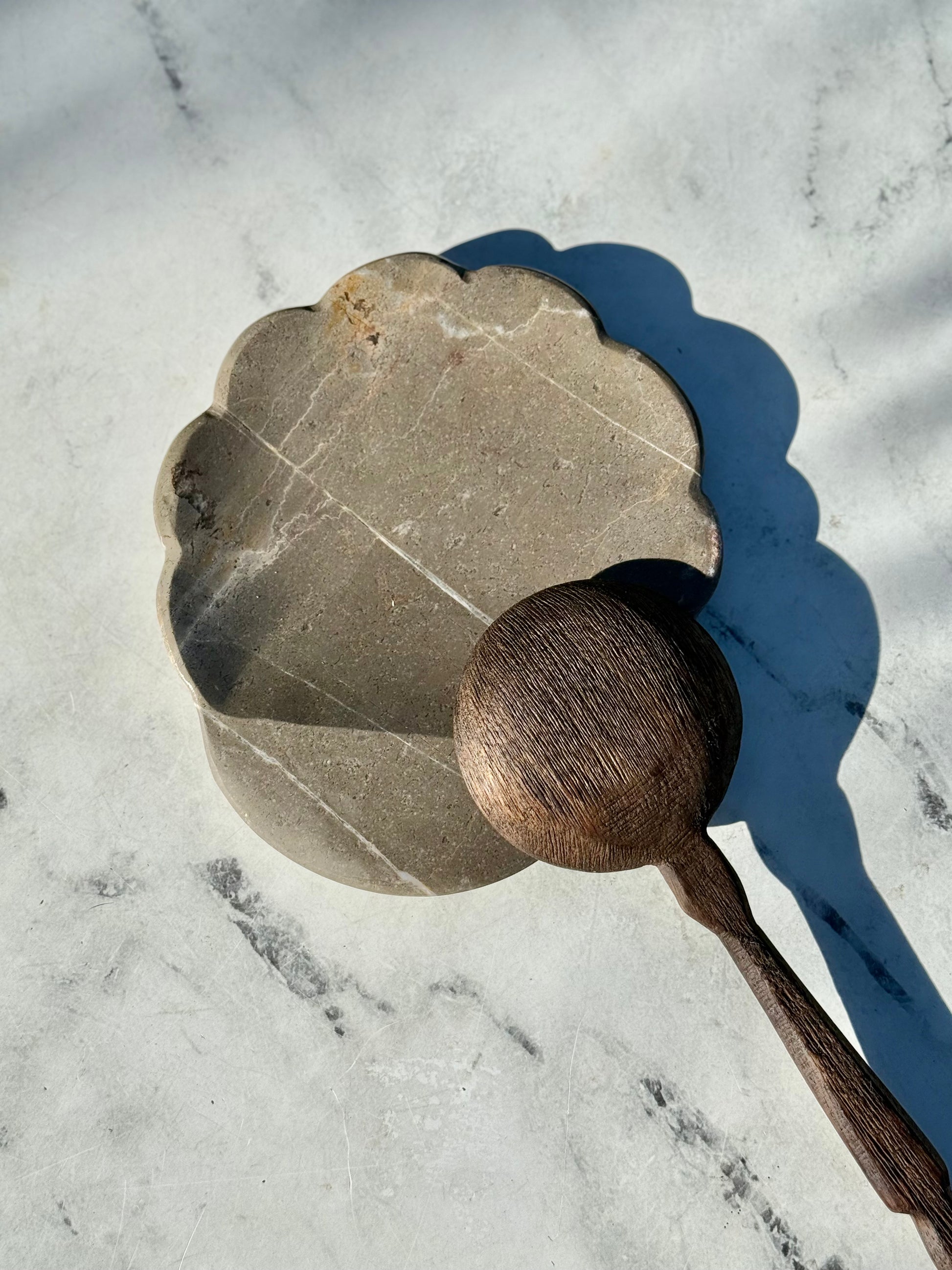 Decorative stone with scalloped edge and wooden ball on a marble surface